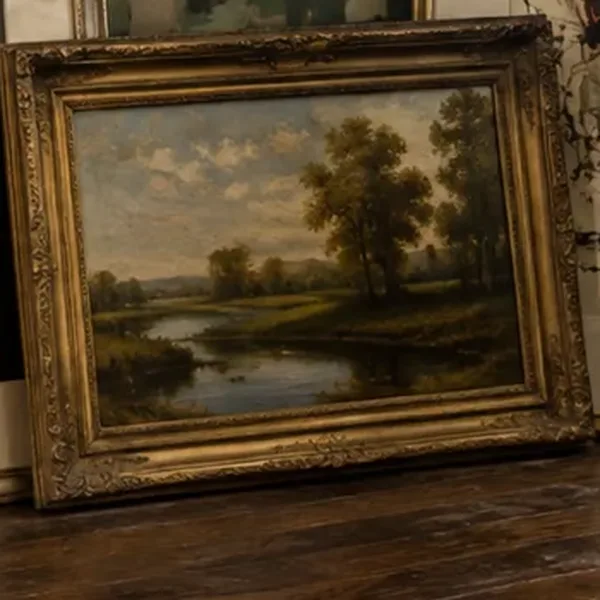 An oil painting of trees and a river in an ornate gilt frame.