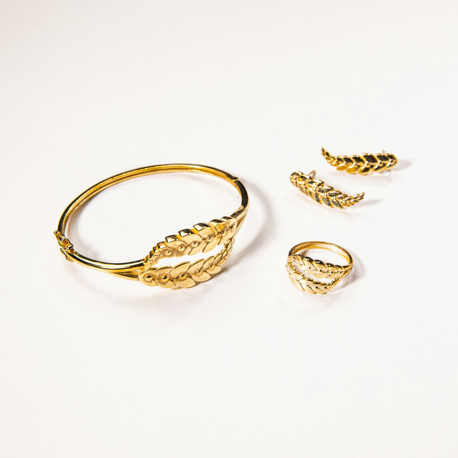 Gold jewelry set featuring leaf designs includes bracelet, ring, and earrings.